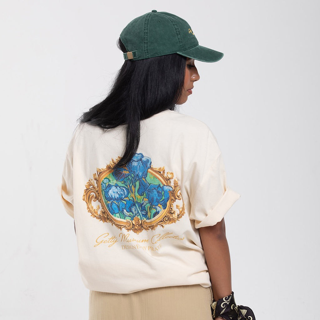 Person wearing a cream-colored t-shirt with a decorative design and a green cap on a white background