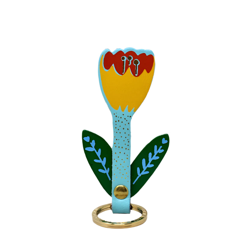 A leather keychain with a hand-painted floral design in blue, yellow, and red, featuring gold-plated hardware, displayed against a neutral background.