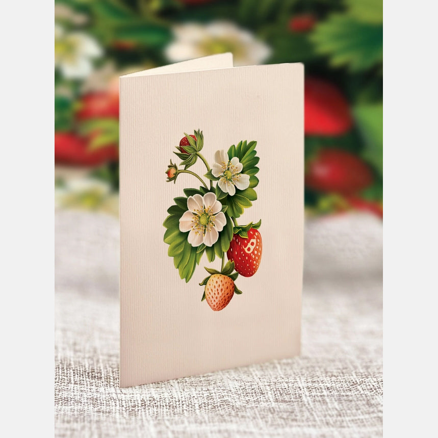 Card with strawberry design on a textured surface with blurred strawberries in the background