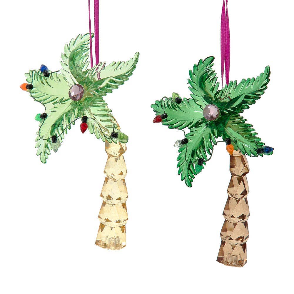 Two Christmas tree ornaments shaped like palm trees, one with a light green trunk and the other with a tan trunk, both with green fronds, hanging pink ribbons, and small multicolored holiday lights, shown on a white background.