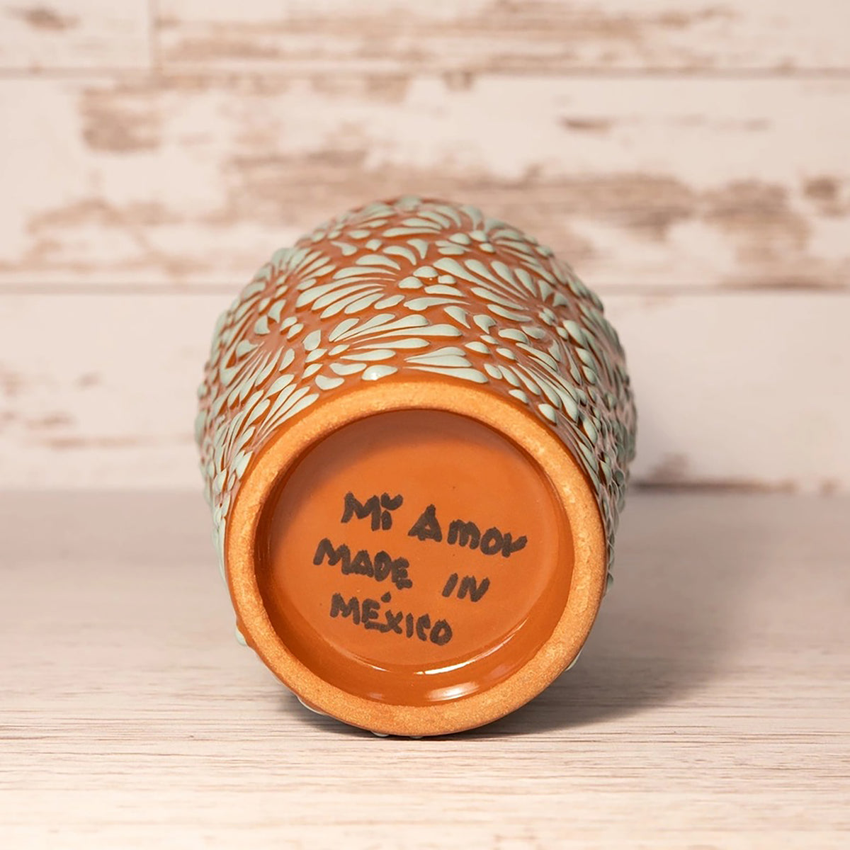Ceramic vase with floral pattern and 'Mi Amor Made in Mexico' text on a wooden surface.