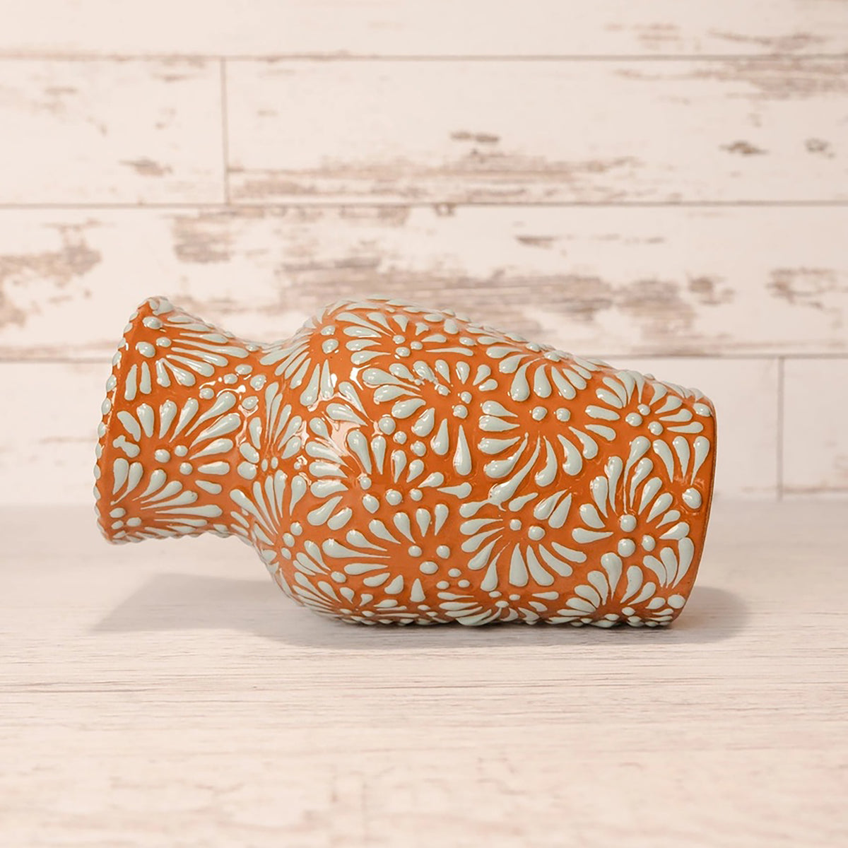 Decorative vase with orange and white floral pattern on a wooden surface