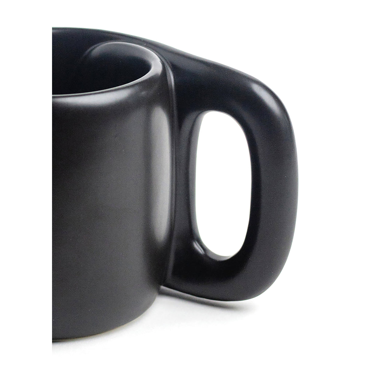 Close-up of a matte black ceramic mug with a uniquely shaped integrated handle, shown against a plain white background.