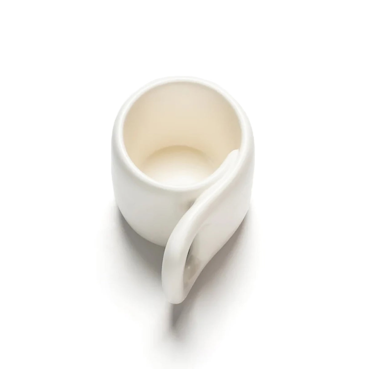 A minimalist white ceramic mug with a unique, integrated side handle, shown from an elevated angle on a clean white background.