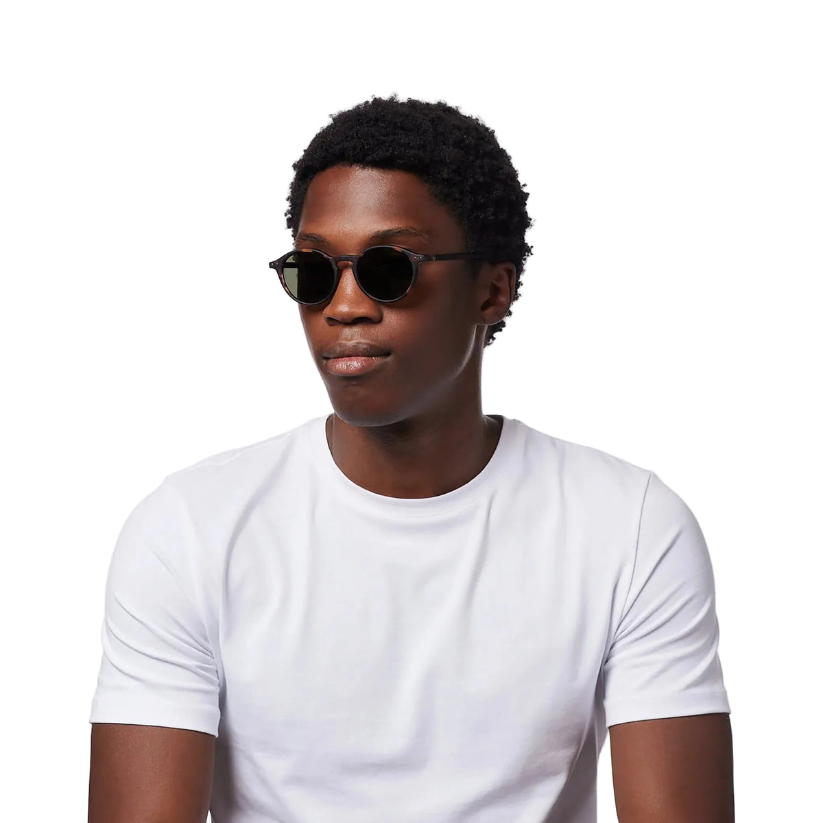 A man wearing round dark sunglasses and a plain white t-shirt, photographed against a clean white background.