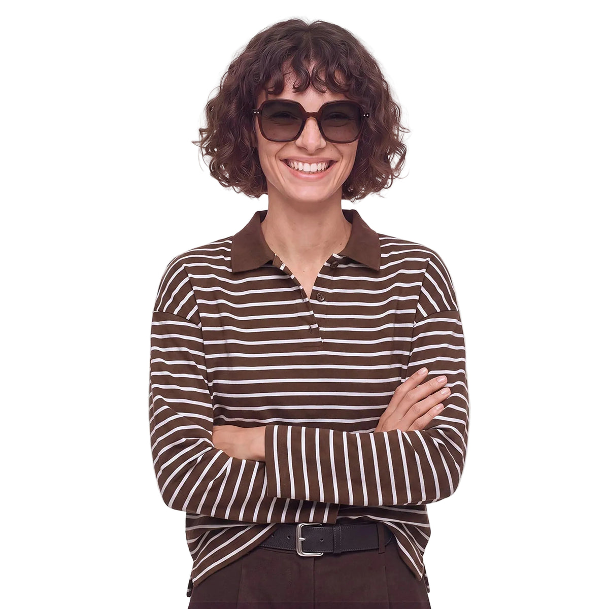 A woman with short curly brown hair and sunglasses, wearing a brown and white horizontally striped long-sleeve polo shirt with a brown collar, standing with arms crossed against a plain white background.