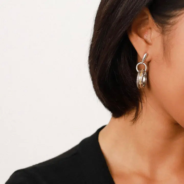 Close-up of a person wearing silver hoop earrings with a plain background