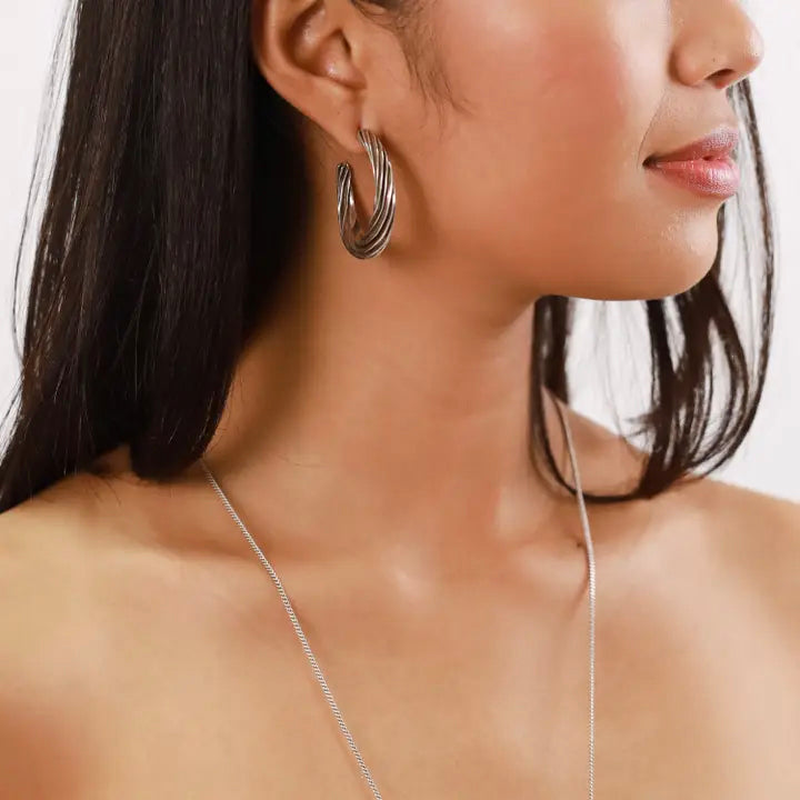 Close-up of a woman wearing silver hoop earrings and a necklace on a plain background