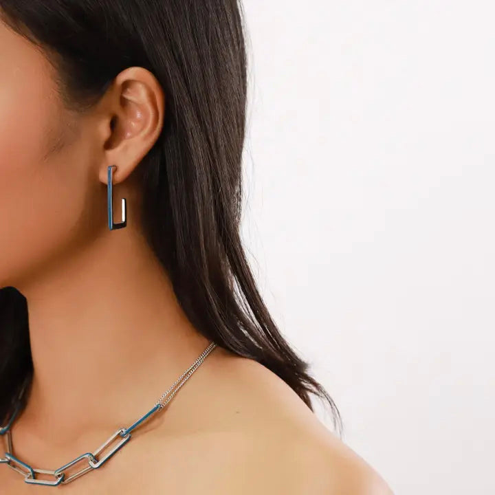 Close-up of a person wearing a silver earring and necklace on a plain background