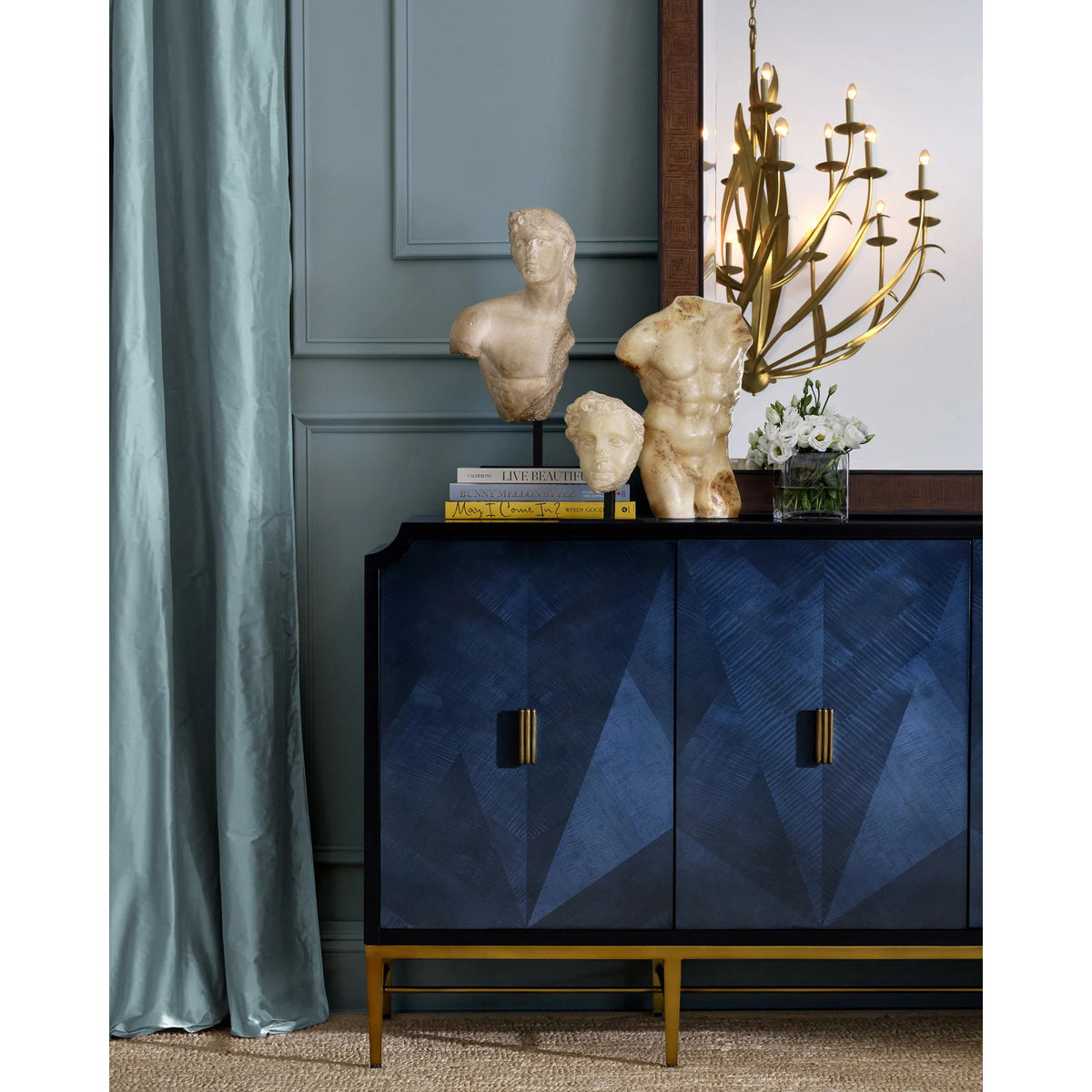 Blue cabinet with geometric design, gold accents, and decorative items in a room with a chandelier.