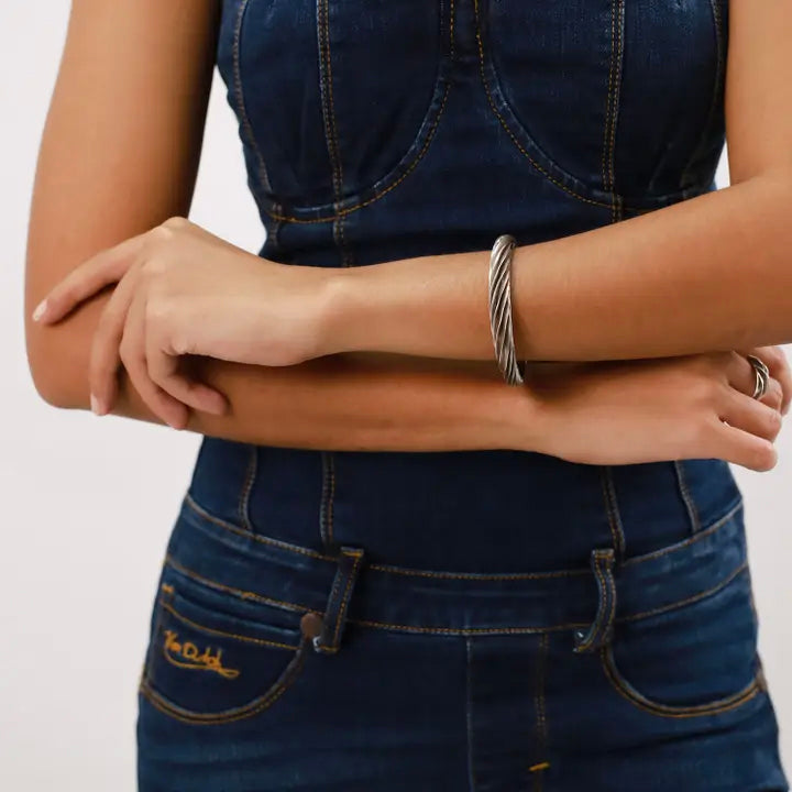 Person wearing a denim outfit with a silver bracelet and ring on a plain background