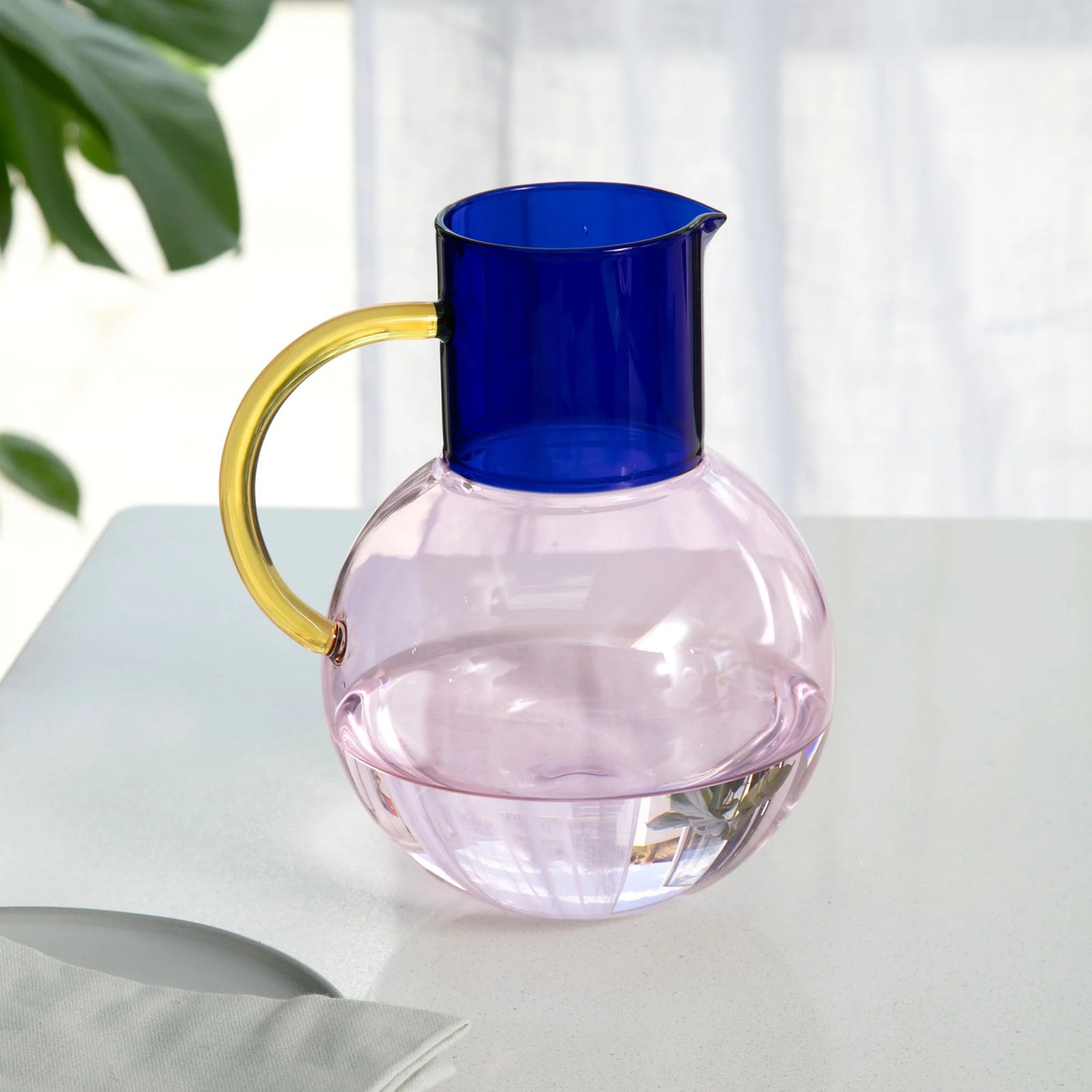 Colorful glass pitcher with blue top, pink base and yellow handle on a white background
