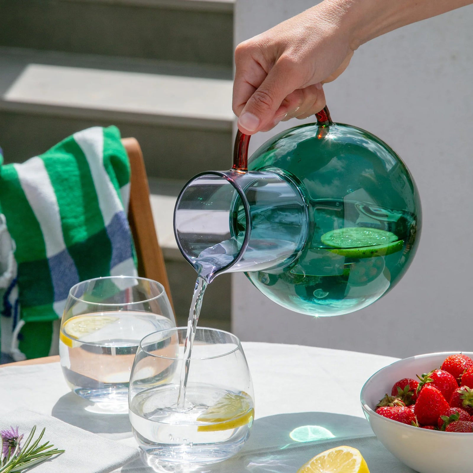 Purple and green glass pitcher with a red handle on a white background