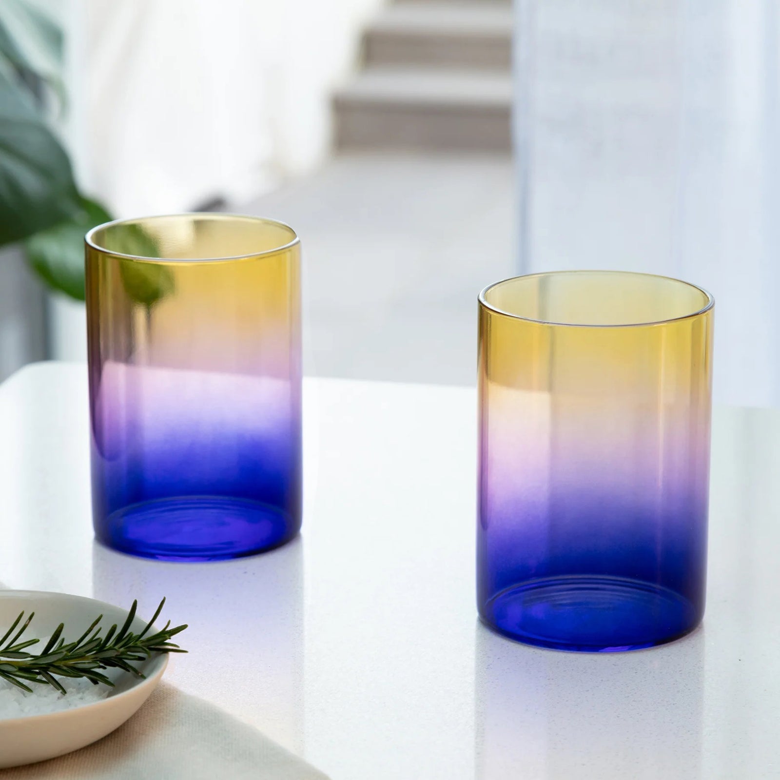 Gradient glass tumbler transitioning from yellow to blue on a white background