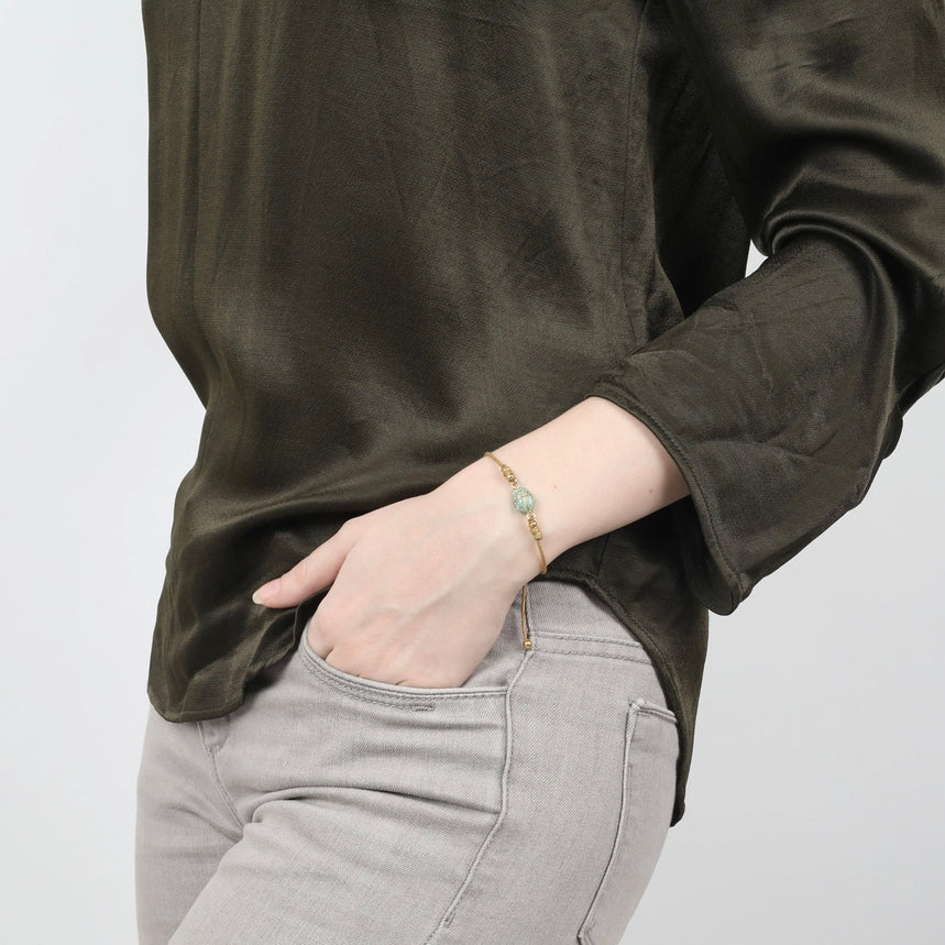 Gold bracelet with a green bead on a white background