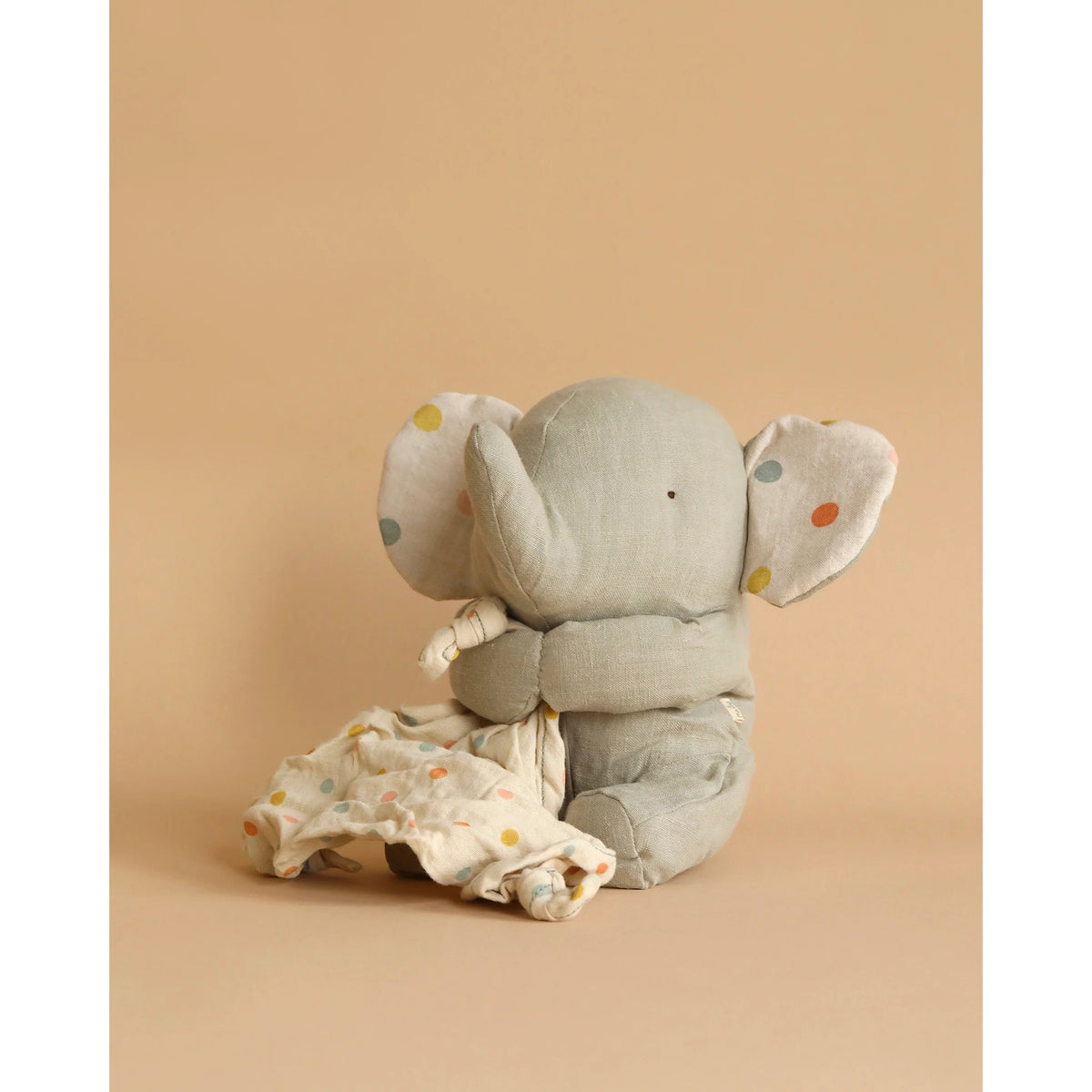 Gray elephant plush toy with a small bag on a beige background