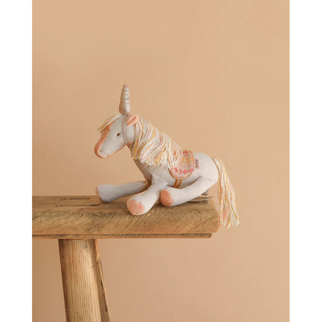 Stuffed unicorn toy on a wooden table against a beige background