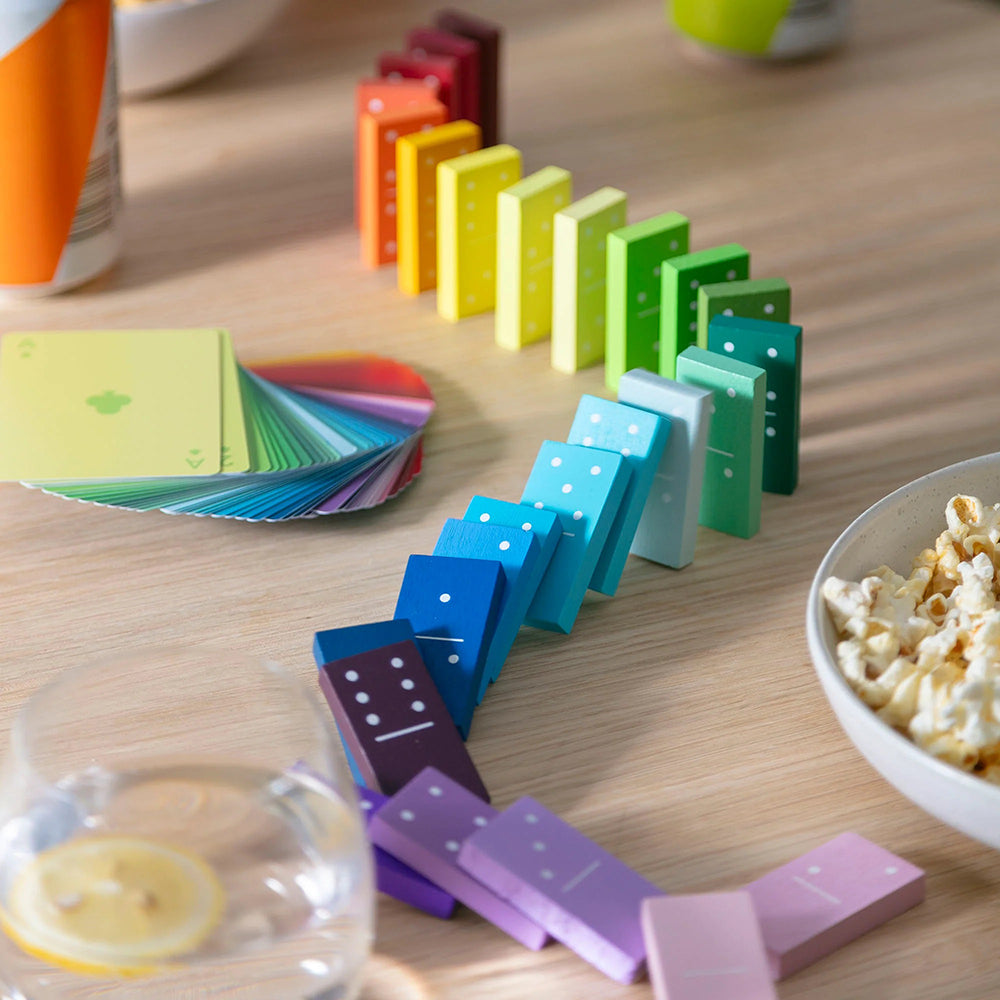 Colorful dominoes in the process of falling down on a wooden table surrounded by snacks and beverages 