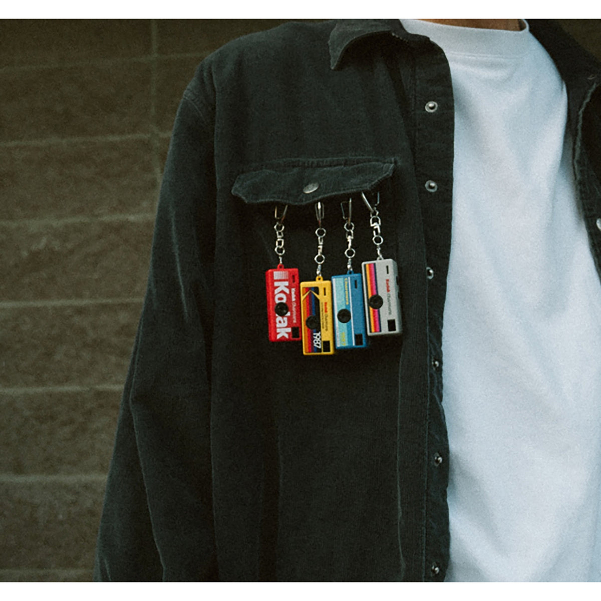 Person wearing a dark jacket with colorful mini camera keychains hanging from the pocket.