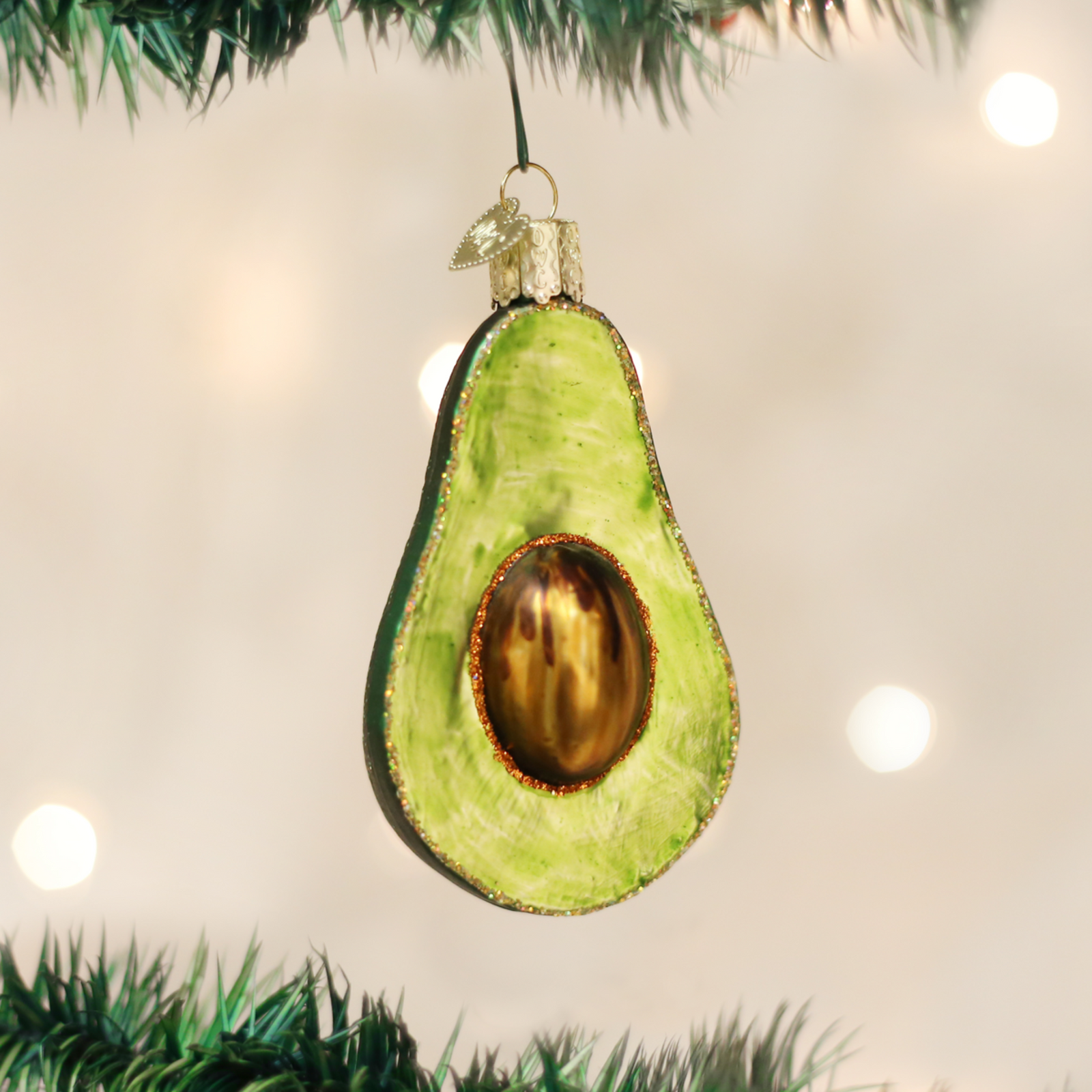 An avocado-shaped Christmas ornament with a textured green body, a metallic gold-brown pit, and a silver hanging loop on a plain white background.