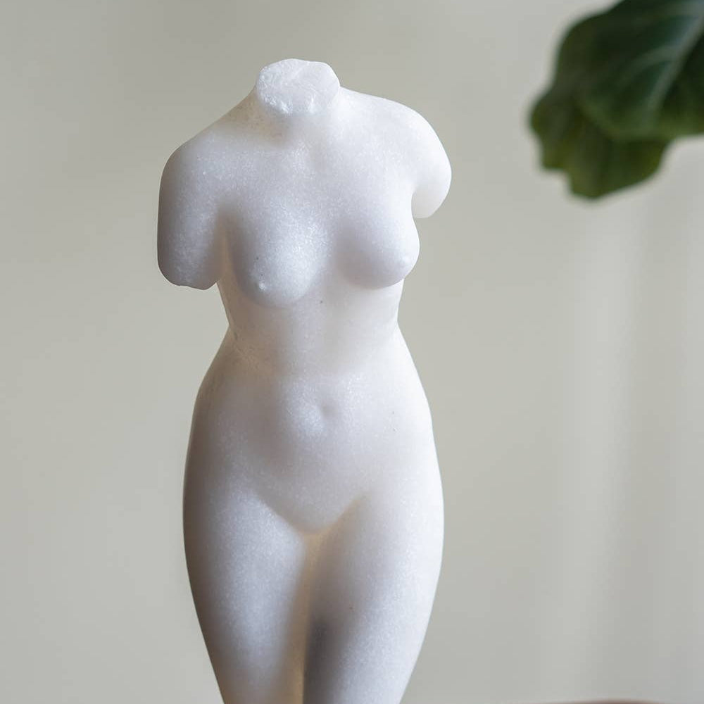 White marble sculpture of a female torso on a stand with a neutral background