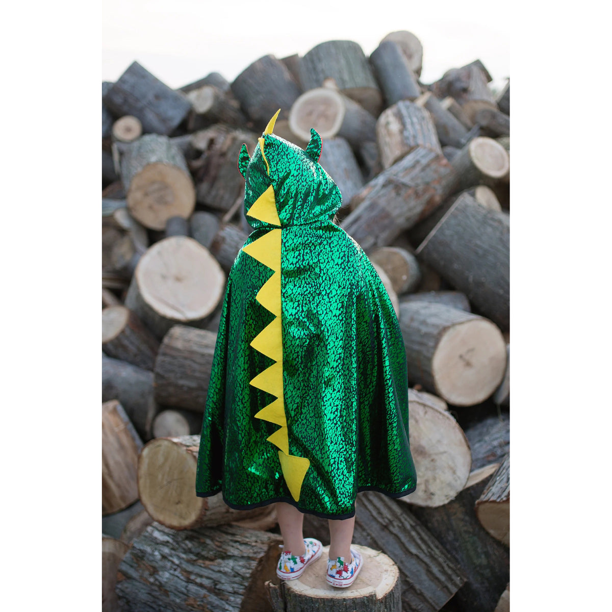 Child wearing a green dragon costume with yellow accents standing on a stack of logs.