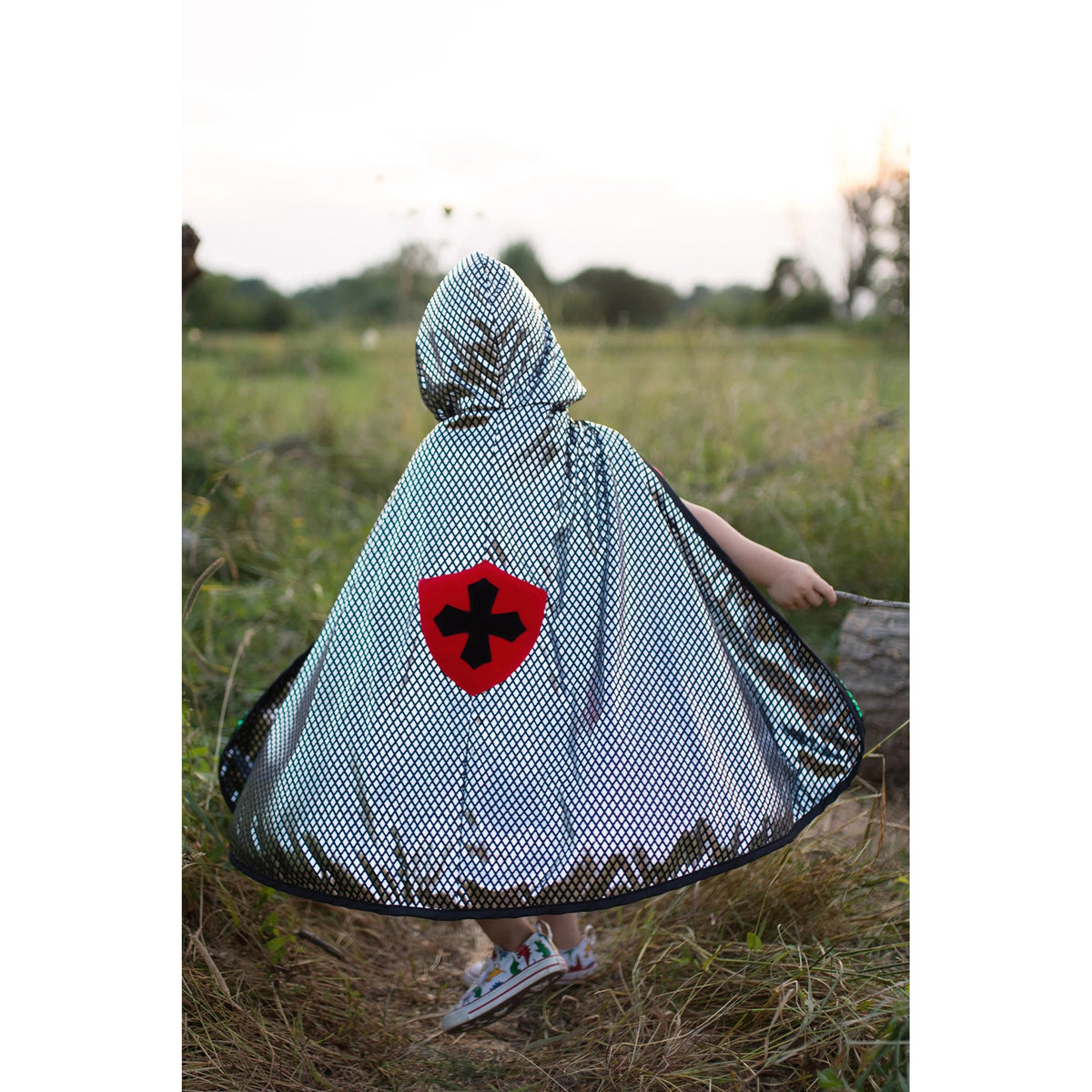 Child wearing a hooded cape with a red emblem in a grassy field