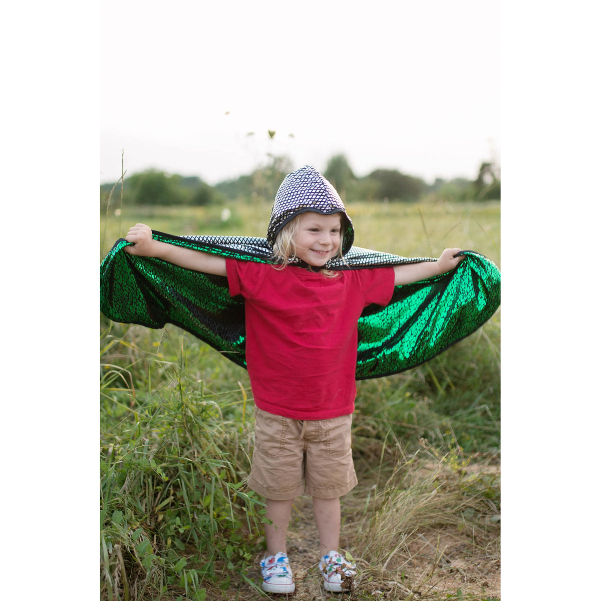 Child holding a green sequin cape outdoors in a field