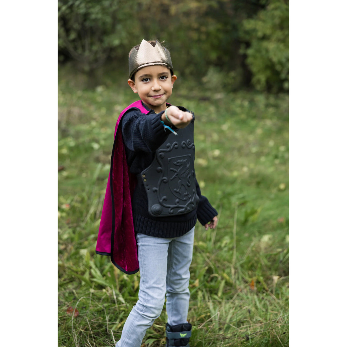 Child in a costume with a helmet and cape standing in a grassy field.