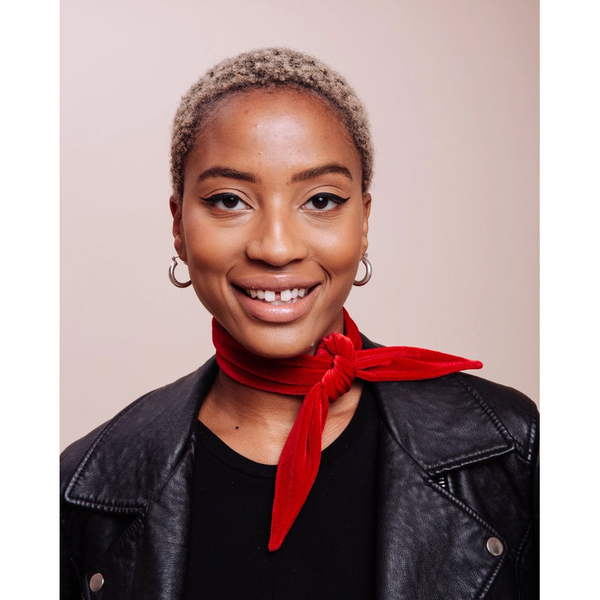 Woman wearing a black leather jacket and red scarf against a beige background