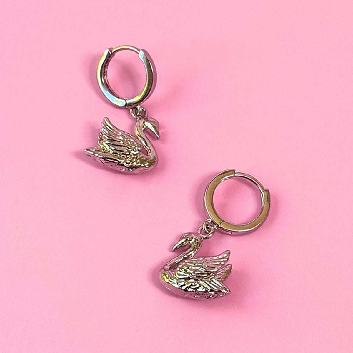 Silver swan-shaped earrings on a pink background