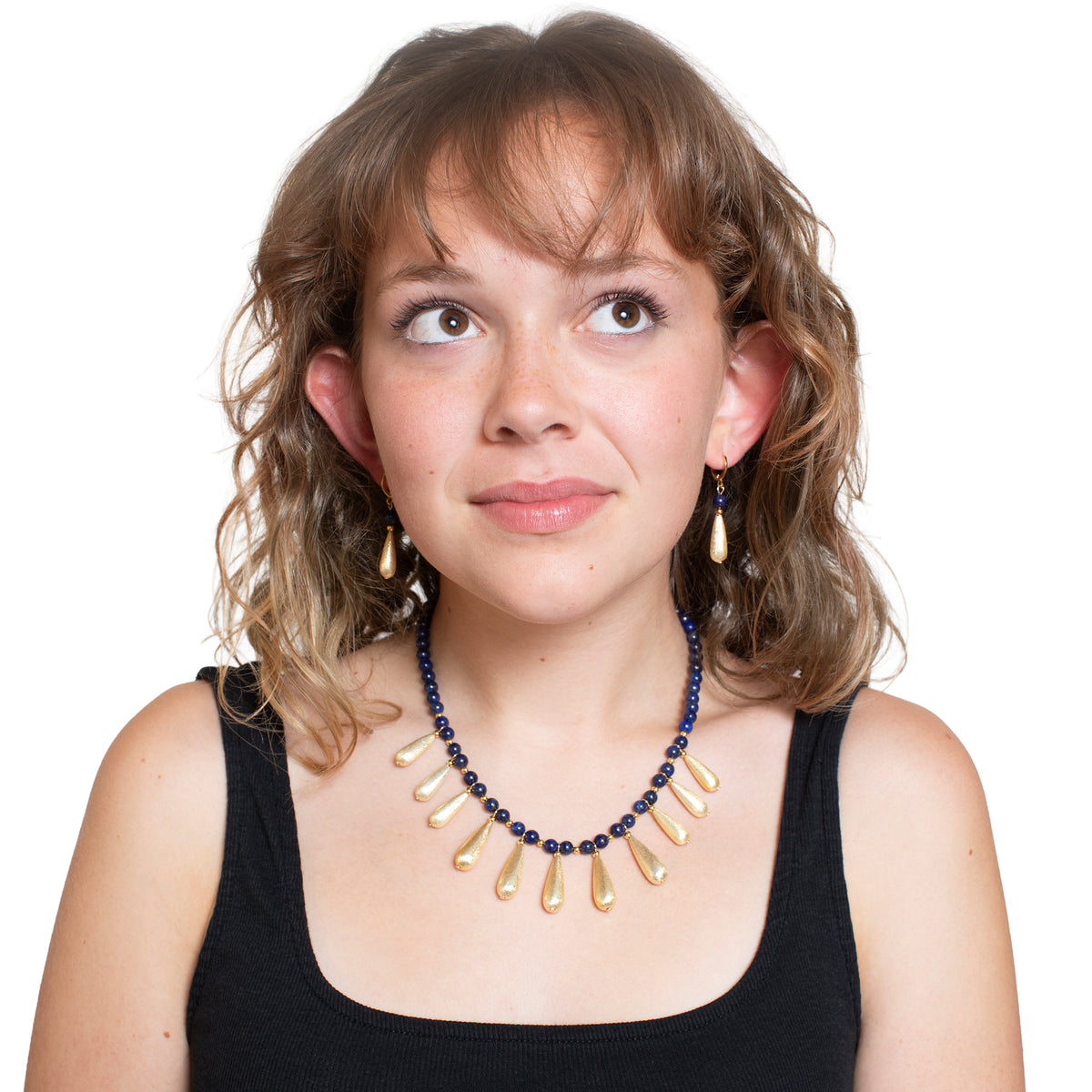 Woman wearing a black top and a blue and gold necklace on a white background
