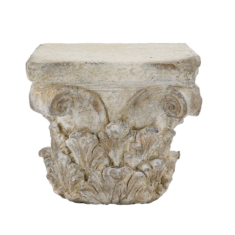An ornate classical column capital stone or faux-stone decorative accent piece with carved acanthus leaves and scrollwork, shown on a plain white background.