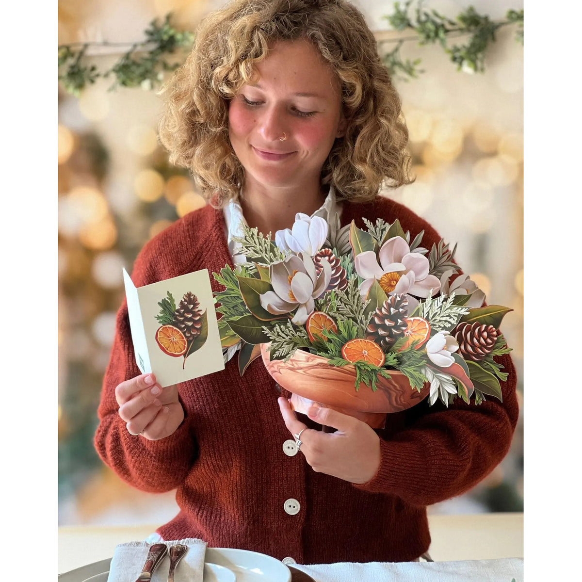 Person holding a bouquet of flowers and a card with a nature-themed design.