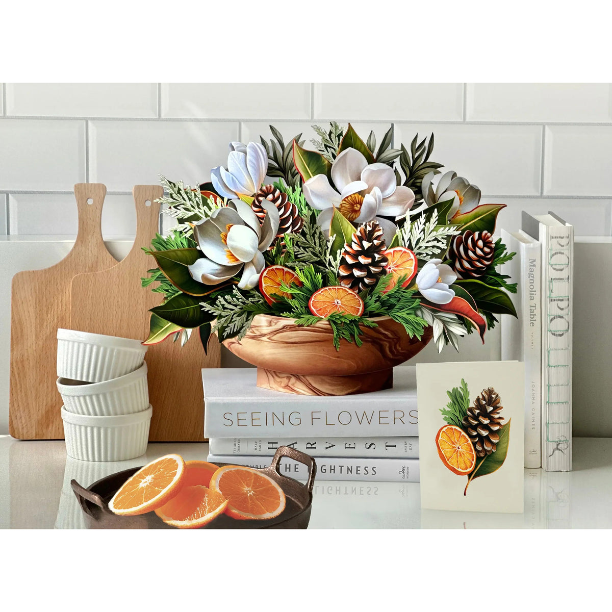 Bouquet of flowers with oranges and pinecones on a kitchen counter.