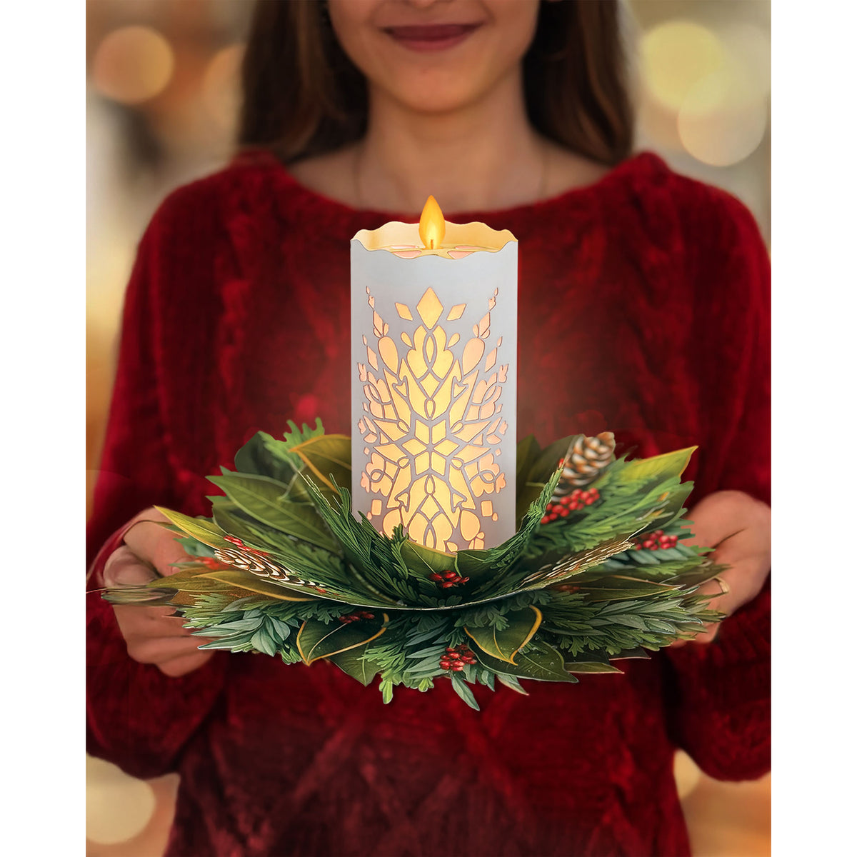 Person holding a decorative candle holder with a lit candle inside, featuring a snowflake design.