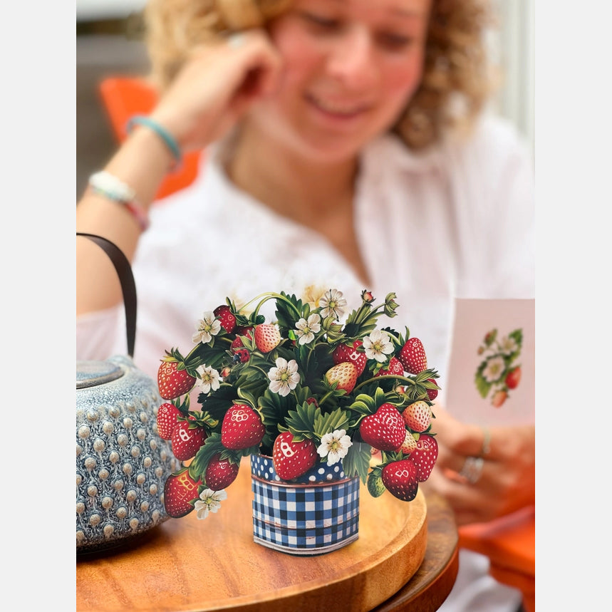 Woman sitting at a table with a decorative strawberry-themed plant and teapot.