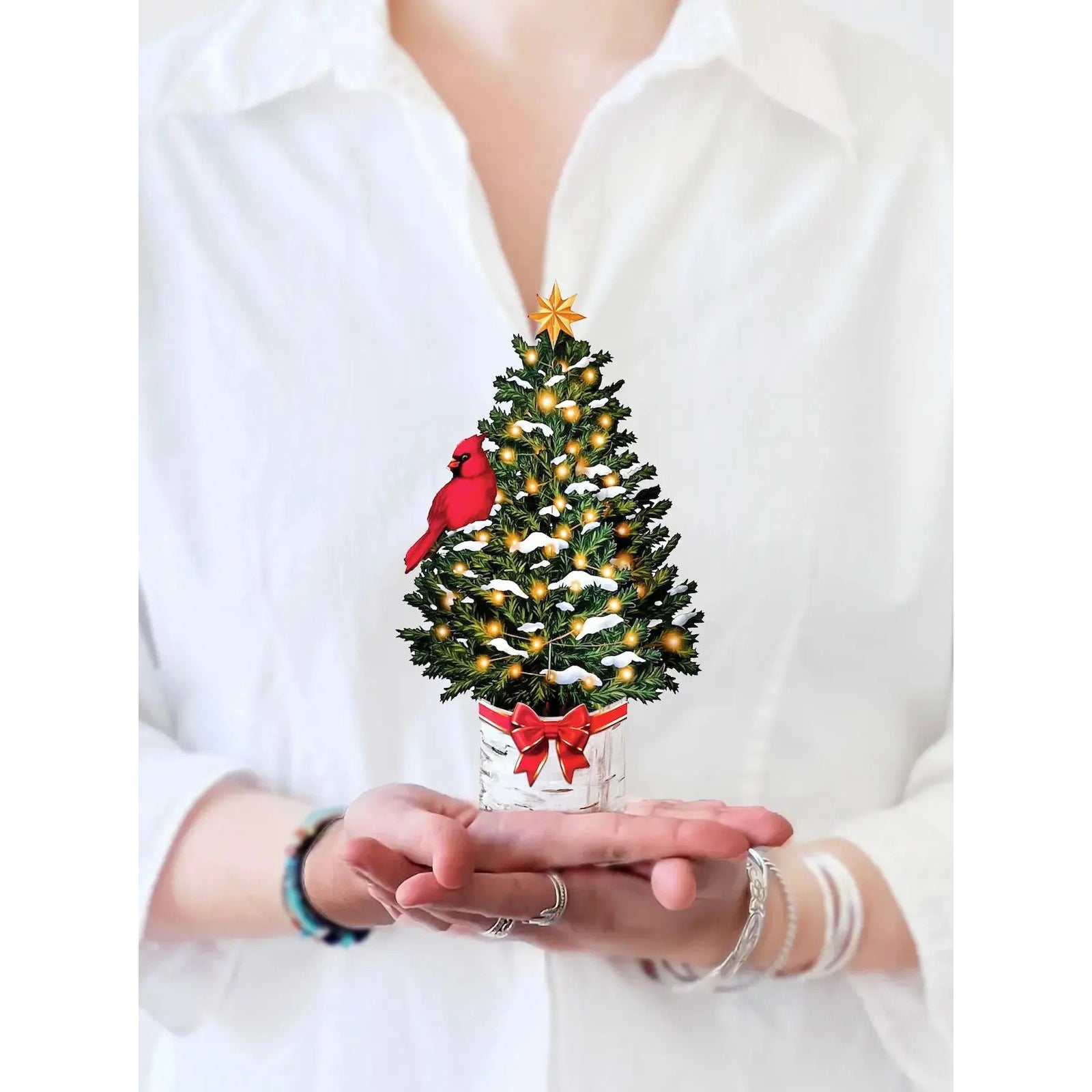 Small decorated Christmas tree held in hands with a white shirt background