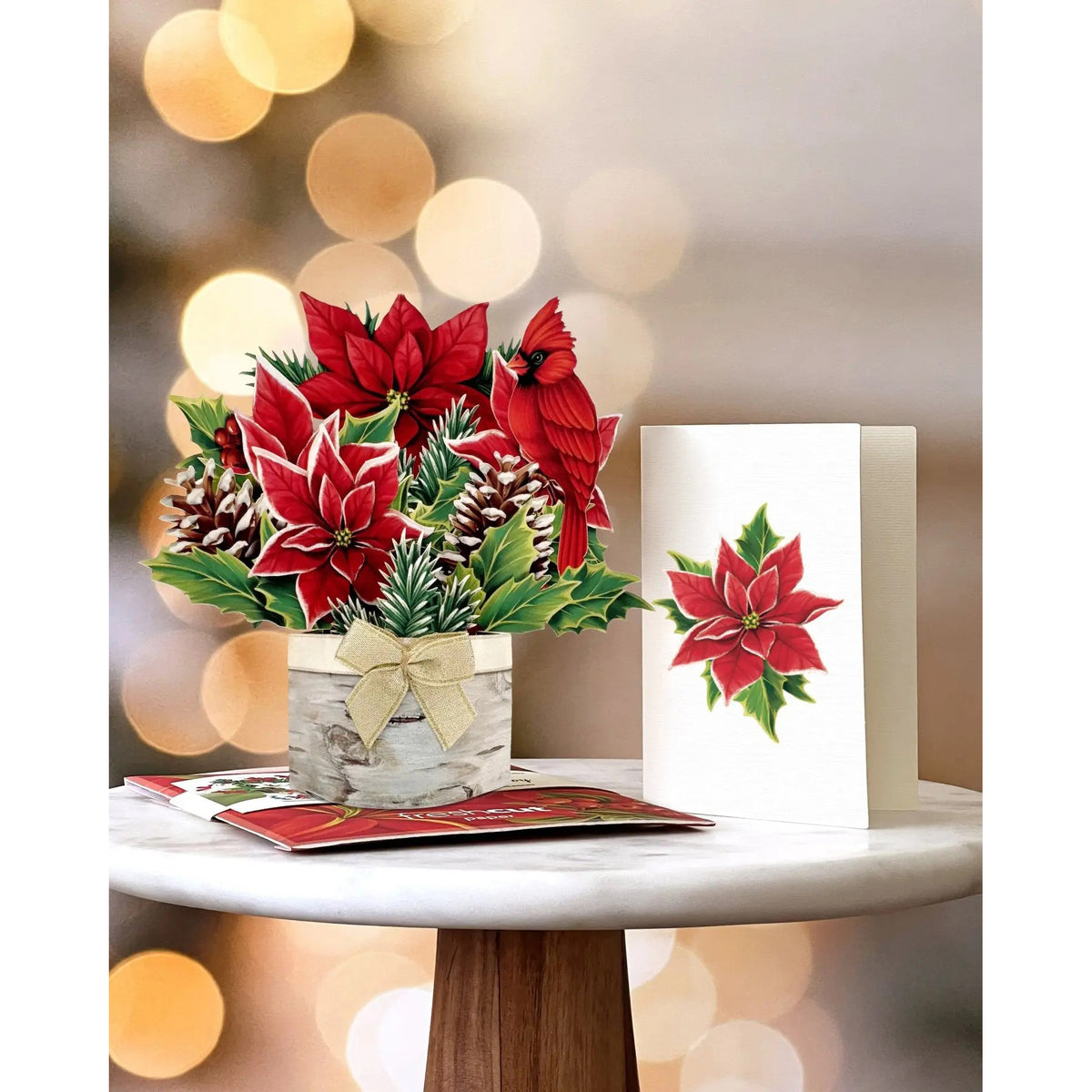 Decorative arrangement with poinsettias and cardinals next to a Christmas card on a blurred background