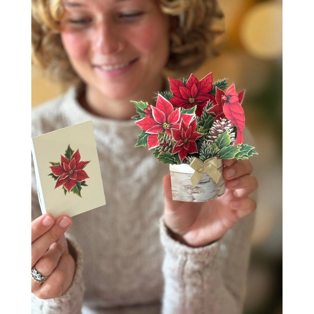 Person holding a small potted plant with red flowers and a matching card.