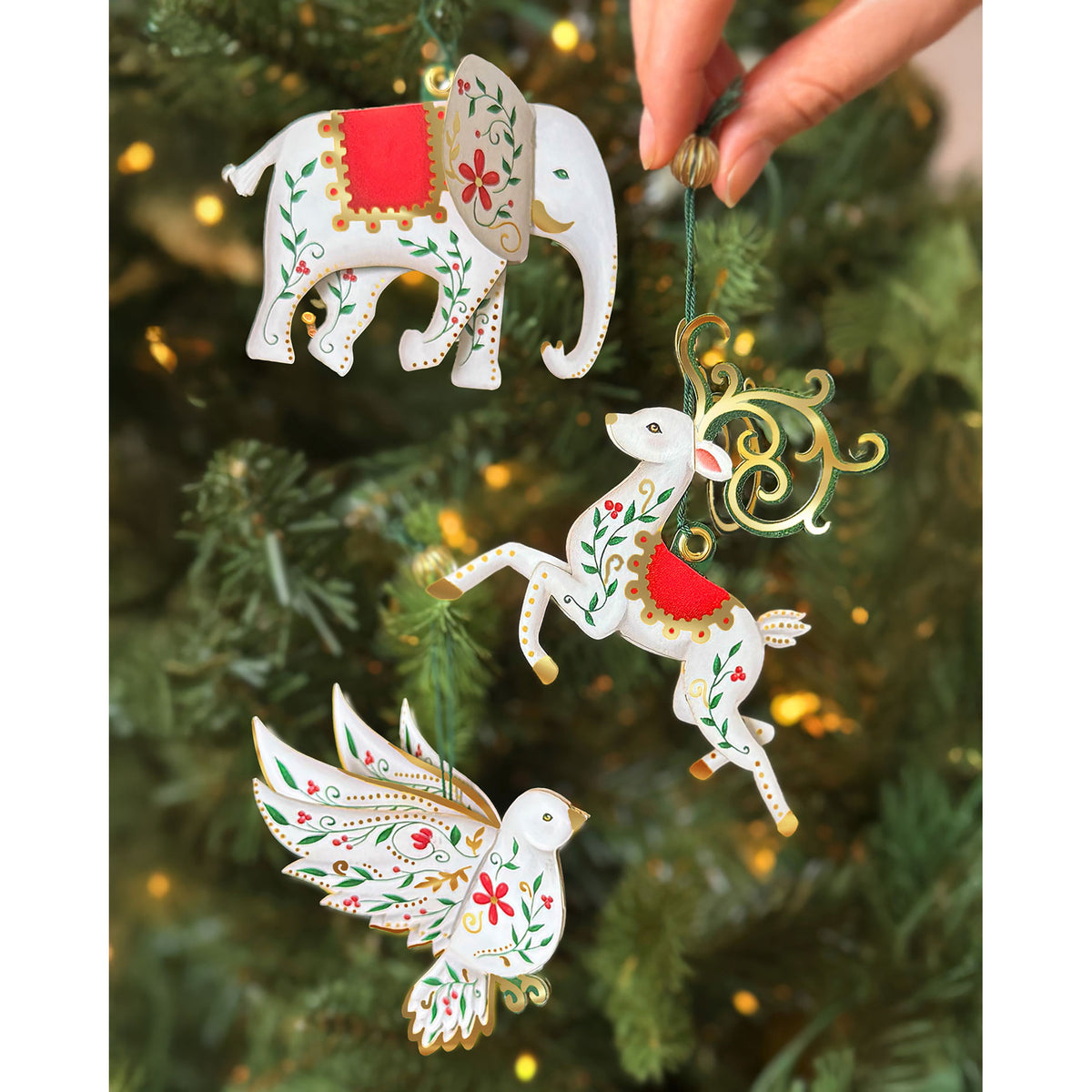 Decorative Christmas ornaments shaped like an elephant, deer, and bird hanging on a tree.