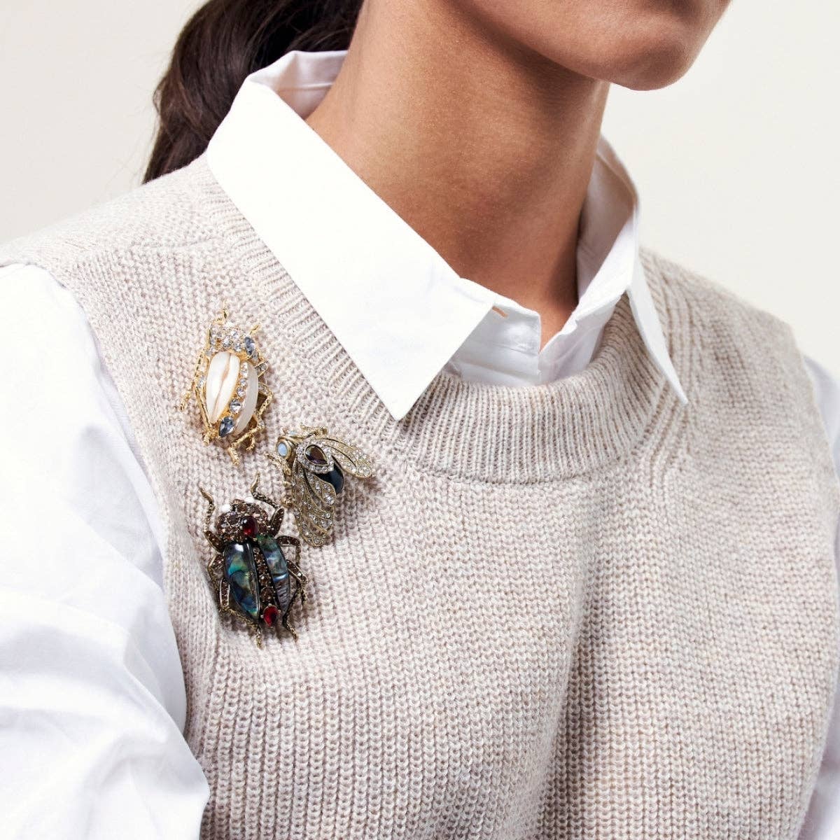 Close-up of a person wearing a beige sweater vest with decorative brooches and a white shirt.