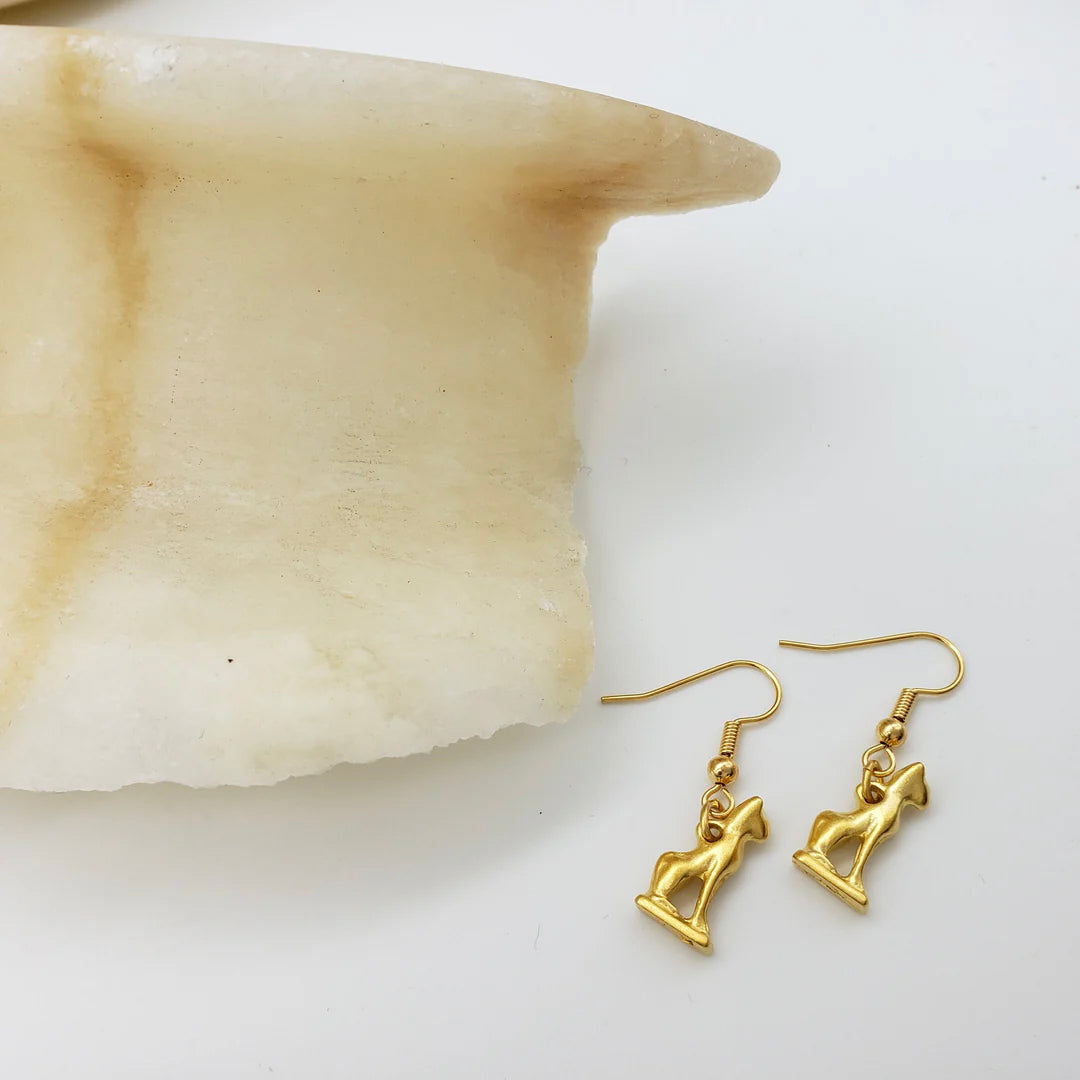 Gold earrings on a white surface with a shell in the background