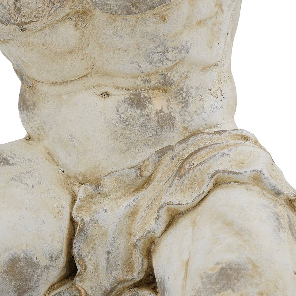 Close-up detail of a classical-style muscular male torso sculpture in a weathered stone finish, showing the chest, abdomen, and draped fabric against a plain white background.