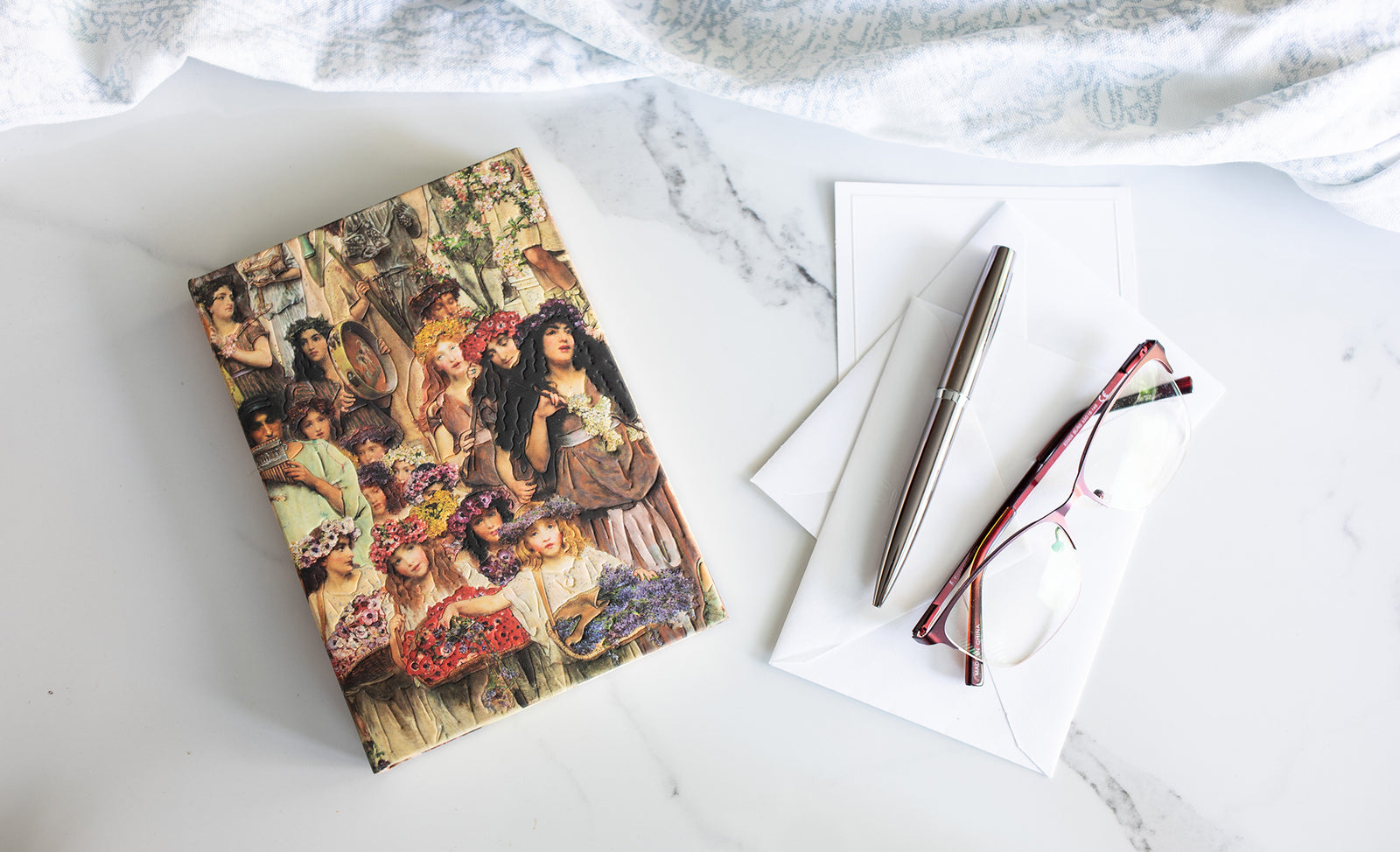 Notebook with artistic cover on a marble surface with a pen and glasses.