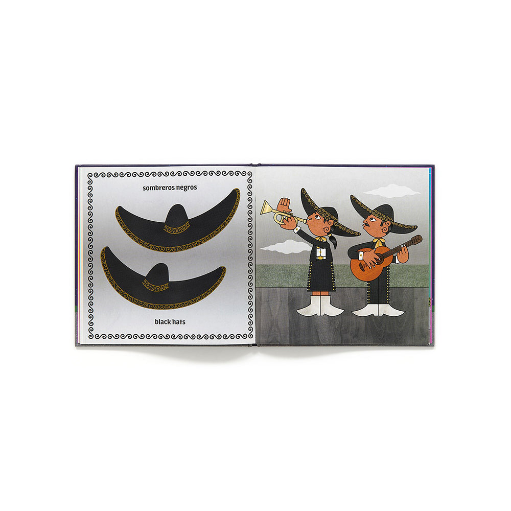 An open children's book spread showing illustrated mariachi hats and two people playing instruments. The left page shows two black sombreros with gold trim labeled 'sombreros negros' and 'black hats.