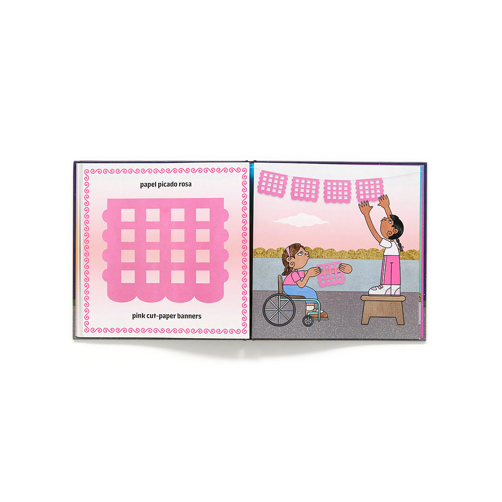 An open children's book on a white background. The left page shows a pink grid labeled 'papel picado rosa' and 'pink cut paper banners,' while the right page features an illustration of a child in a wheelchair hanging pink patterned banners outdoors.