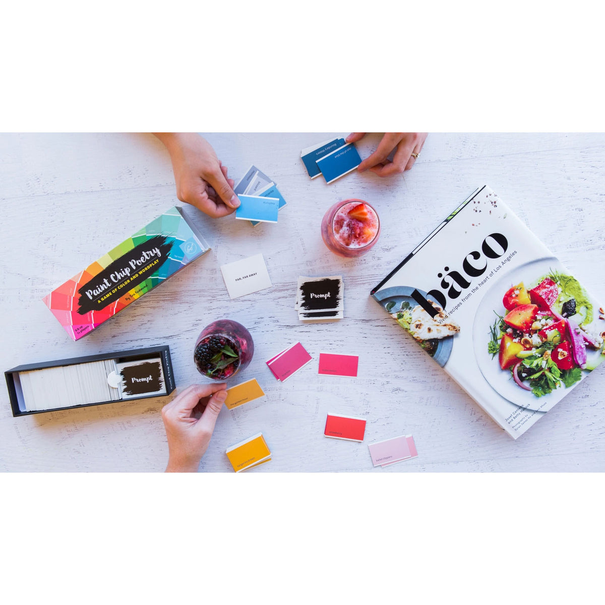 People playing a game with colorful cards and a book on a white surface