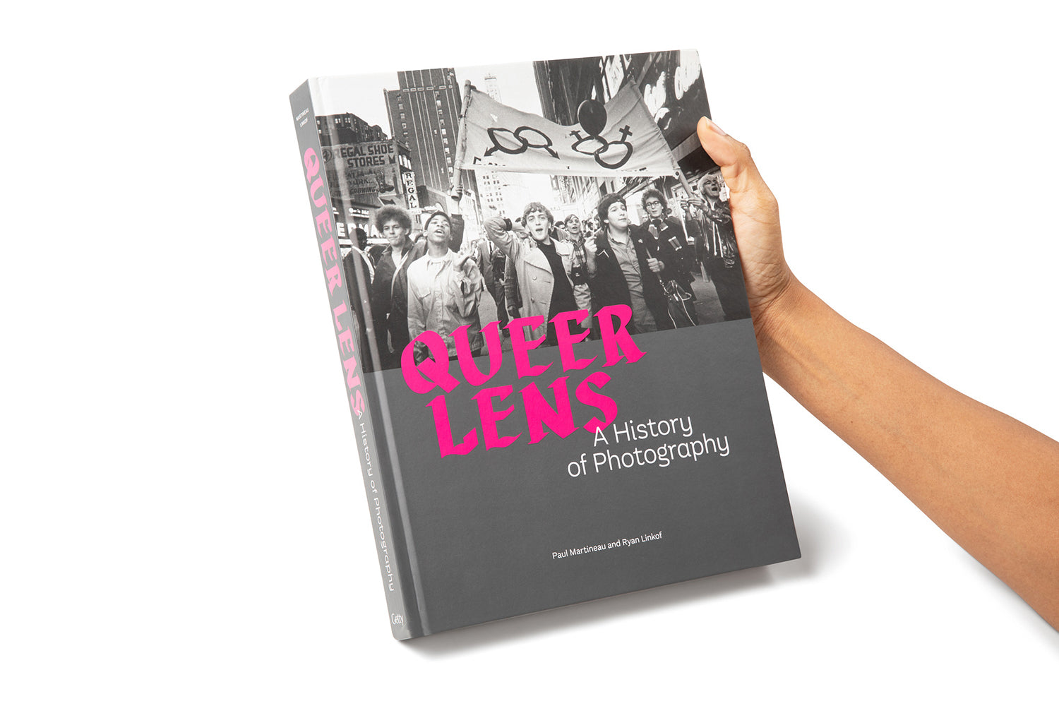 Cover of the book 'Queer Lens: A History of Photography' featuring a black and white photograph of a protest with the title text overlaid in pink.
