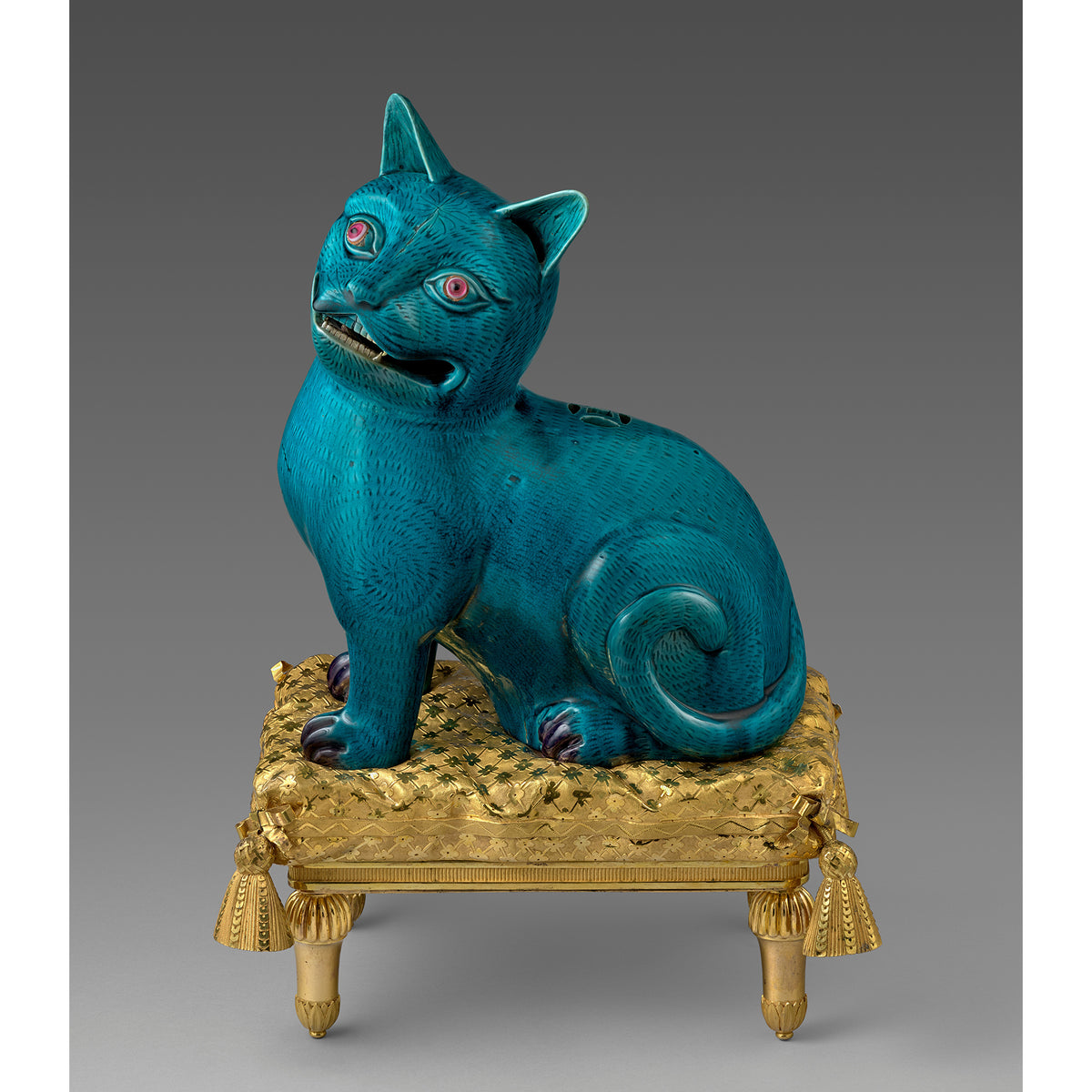 Blue cat figurine on a gold pedestal against a gray background